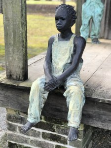 Statue depicts a Black child in yellow clothes, seated, who was enslaved at the Whitney Plantation near New Orleans, LA.