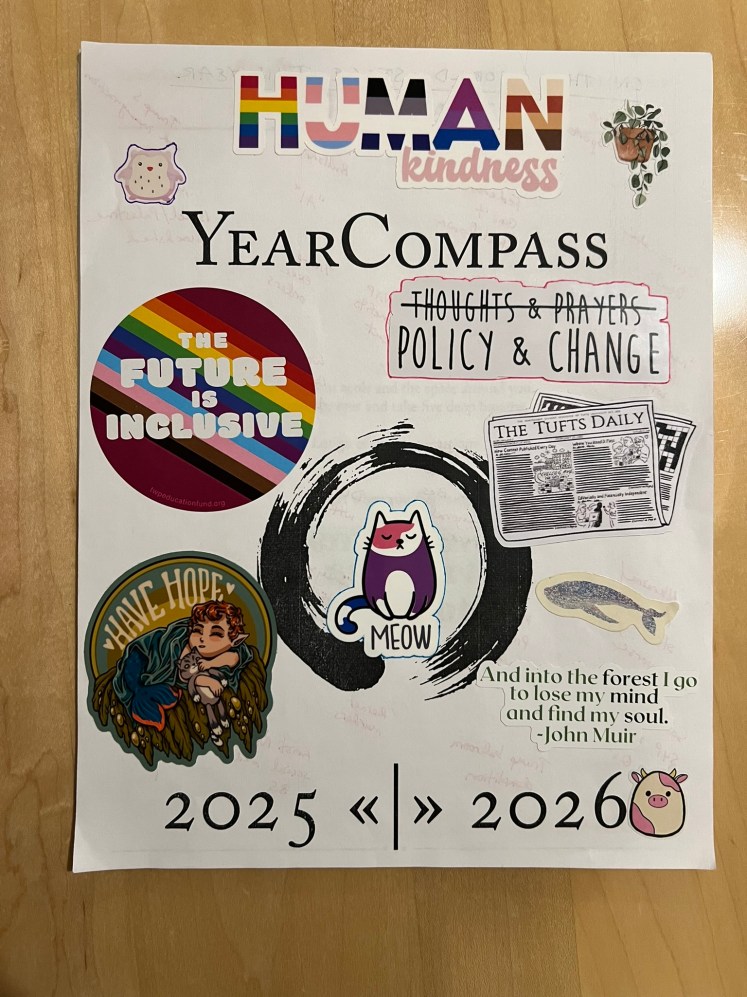 A white piece of paper that has "Year Compass: 2025 2026" printed on it. There are many stickers added to this cover, as well: a multicolored "HumanKindness" sticker in the colors of many types of LGBTQAI+ flags, a chibi owl and chibi cow, a purple and pink cartoon cat that says "meow," a rainbow circle that says "The future is inclusive," a cartoon mermaid, sleeping with a stuffed animal, which says "have hope," a cartoon sticker of The Tufts Daily newspaper, a whale, a plant, printed words "Thoughts and Prayers" (crossed out) with "Policy and Change" written below in larger type, and a quote from John Muir that says "And into the forest I go to lose my mind and find my soul."